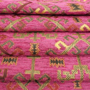May include: Close-up of pink fabric with a woven geometric pattern in gold, brown, and black. The fabric is folded in layers, showing the intricate design.