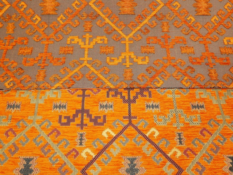 May include: Close-up of a patterned fabric with a geometric design in shades of orange, brown, and gray. The fabric has a textured surface and a woven appearance.