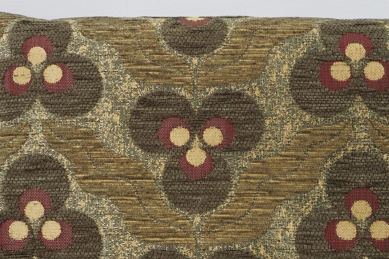 May include: Close-up of a decorative pillow with a repeating floral pattern. The design features dark brown, textured circles with red and cream-colored accents. The background has a woven, textured appearance in shades of brown and gold.
