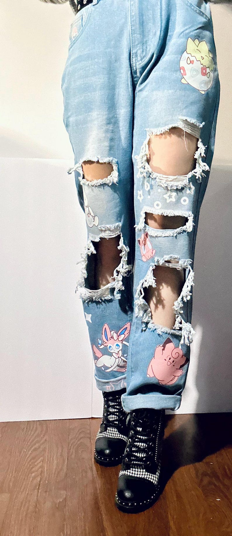 Puede incluir: Vaqueros azul claro con roturas y dise&ntilde;os de personajes de dibujos animados coloridos. Los vaqueros tienen m&uacute;ltiples roturas. Se combinan con botas de combate negras.