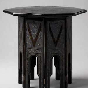 May include: A dark, octagonal side table with intricate geometric patterns. The table features a dark finish with decorative panels and a detailed design on the tabletop. The legs are arched and the table is approximately 24 inches tall.