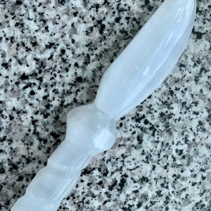 May include: White selenite crystal wand with a twisted handle. The wand is smooth and polished, with a slightly pointed tip.