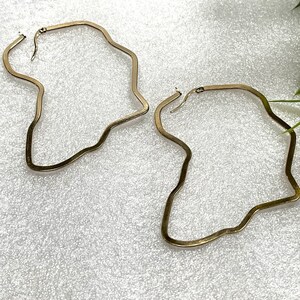Op de afbeelding: Een paar gouden oorringen met een onregelmatige, golvende vorm.