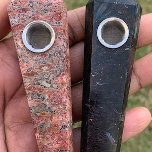 May include: Two crystal pipes, one red and one black, with metal screens. The pipes are shaped like points and are held in a hand.