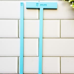 May include: Two blue plastic rulers, one with a T-shaped handle and the text "8 mm" printed on it, and the other a straight ruler.