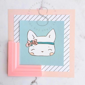 May include: A cute illustration of a white cat face with a floral headband and a teal band. The cat is on a light blue background, layered with a striped paper and a pink frame. The image is a square composition.