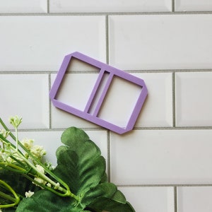 May include: A purple plastic double-sided picture frame with a rounded rectangular shape.