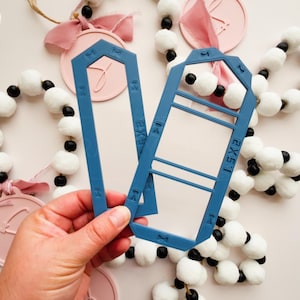 Può includere: Due cornici di plastica blu, una tenuta in mano, con il testo "2X5.1" e "FX+". Le cornici sono circondate da una ghirlanda di pompon bianchi e neri ed etichette circolari rosa con la lettera "J".