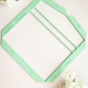 May include: A light green plastic template for making envelopes. The template has the words "Crafty Friend" printed on it and markings for folding the envelope.