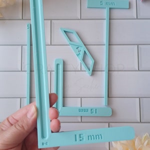 May include: A set of three light blue plastic rulers with measurements in millimeters. The rulers are shaped like a T, an L, and a straight line. The rulers are 5 mm, 15 mm, and 51 mm long.