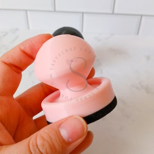 May include: Pink and black craft tool with the text "Easy Scrap For You" on the side. The tool has a round, flat base and a raised, rounded top.