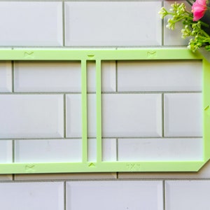 May include: A light green plastic frame with a vertical divider in the center. The frame is on a white tiled surface.