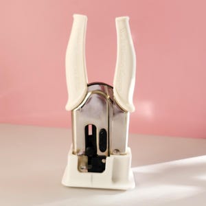 May include: White metal hole punch with white plastic handles. The handles have the text "We R Memory Keepers" printed on them.