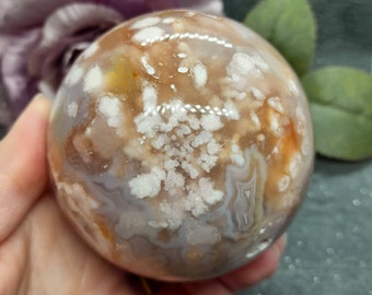 May include: A large, round, agate sphere with a white, brown, and orange pattern. The sphere is polished and has a smooth surface.