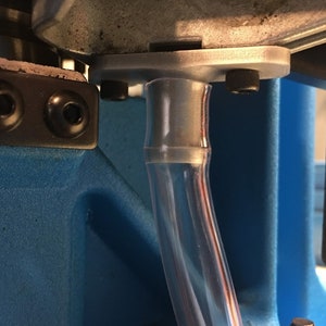 Puede incluir: Primer plano de un tubo de plástico transparente conectado a un soporte de metal plateado. El soporte está unido a una superficie azul.