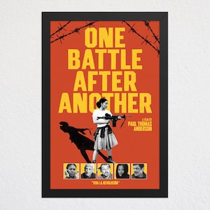 May include: A framed movie poster titled One Battle After Another with a bright orange background. It features a central figure holding a rifle, barbed wire at the top, and five small portraits at the bottom with the text Viva La Revolucion.