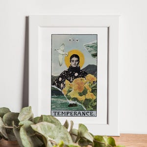 May include: A framed art print featuring a collage-style design of a woman with a yellow halo, a bird, and yellow flowers. The text "XIV" and "TEMPERANCE" are visible. The frame is white.
