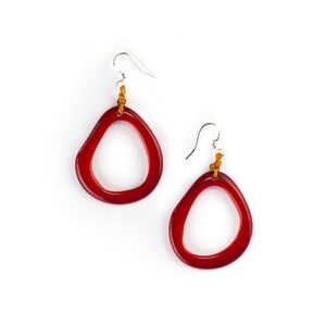May include: A pair of red glass earrings with a unique, organic shape. The earrings are suspended from silver hooks and have brown leather cord accents.