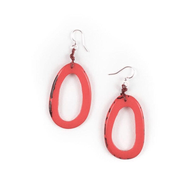 May include: A pair of coral red oval shaped earrings with a silver hook and a brown cord. The earrings are made of a textured material.