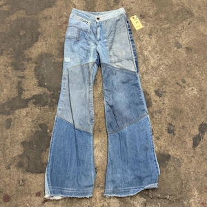 Puede incluir: Vaqueros de mezclilla azul de talle alto con un diseño de parches que combina paneles de tela en tonos azul claro y medio. El pantalón presenta una silueta de pierna ancha, cierre frontal de botón y cremallera, y bajos deshilachados.