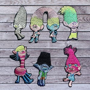 May include: Set of eight embroidered iron-on patches featuring characters from the Trolls movie. The patches are colorful and feature various characters, including Poppy, Branch, and Guy Diamond.