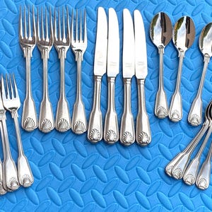 May include: A collection of silver-colored flatware, including forks, knives, and spoons, arranged on a blue textured surface. The flatware features a decorative shell design on the handles. The image showcases a complete set of dining utensils.