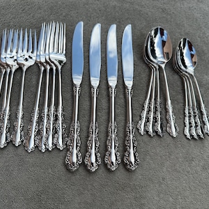 May include: A set of silverware with ornate handles, including forks, knives, and spoons. The silverware is made of polished stainless steel and has a silver finish.
