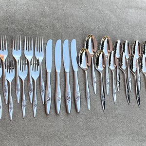 Könnte beinhalten: Ein Besteckset mit floralem Design. Das Set enthält Gabeln, Messer und Löffel. Das Besteck ist aus Edelstahl und hat eine polierte Oberfläche.