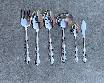 May include: Set of six silver-toned serving utensils with ornate handles. The set includes a fork, two spoons, a ladle, a butter knife, and a small spoon.