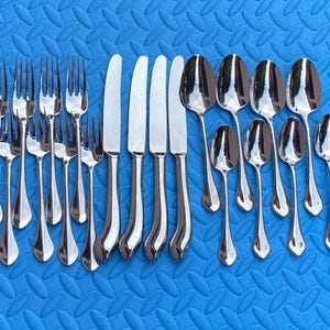 May include: A set of polished cutlery, including forks, knives, and spoons, arranged on a blue surface. The silverware has a reflective, silver finish, and the arrangement suggests a formal dining setting.