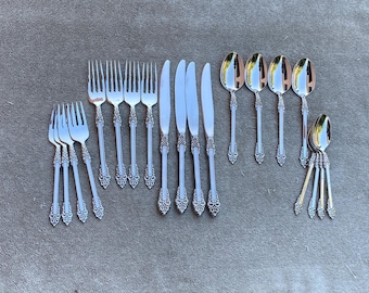 Könnte beinhalten: Ein Set aus silberfarbenem Besteck, bestehend aus vier Menügabeln, vier Kuchengabeln, vier Menümessern, vier Suppenlöffeln und vier kleinen Löffeln. Jedes Teil hat ein dekoratives, geprägtes Schnörkelmuster am Griffende.