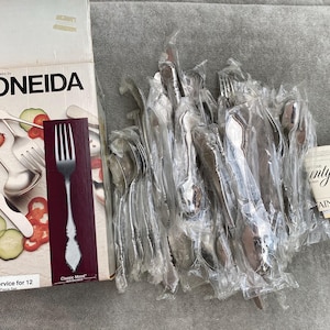 Könnte beinhalten: Ein Set mit 12 Oneida Classic Mood Besteckteilen aus Edelstahl in einzelnen Plastikverpackungen. Die Verpackung ist mit "Service for 12" und "Classic Mood" beschriftet.