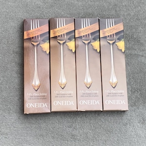 Könnte beinhalten: Vier Schachteln mit Oneida 3-teiligen Bestecksets, jedes mit 18/8 Edelstahl und 24 Karat vergoldet. Jede Schachtel zeigt eine goldene Gabel mit einem dekorativen Design und dem Text "3-Pc Place Setting 18/8 Stainless with 24K Gold Electroplate ONEIDA".