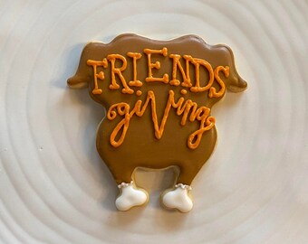 May include: A brown sugar cookie decorated to look like a turkey with the words "Friendsgiving" written in orange icing.