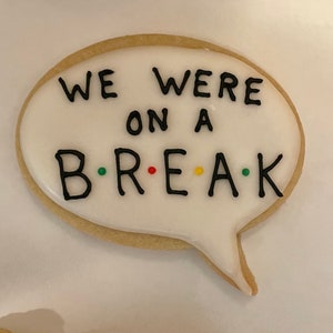 May include: A white cookie decorated with black icing in the shape of a speech bubble. The cookie says "We were on a B.R.E.A.K." with colorful dots between the letters.