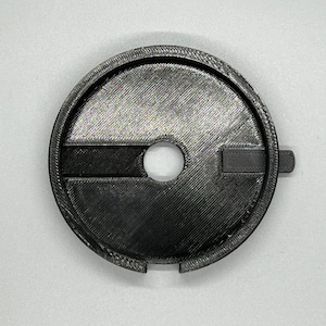 May include: A black plastic 3D printed adapter with a circular shape and a small hole in the centre. The adapter has a raised lip around the edge and a small tab on the side.