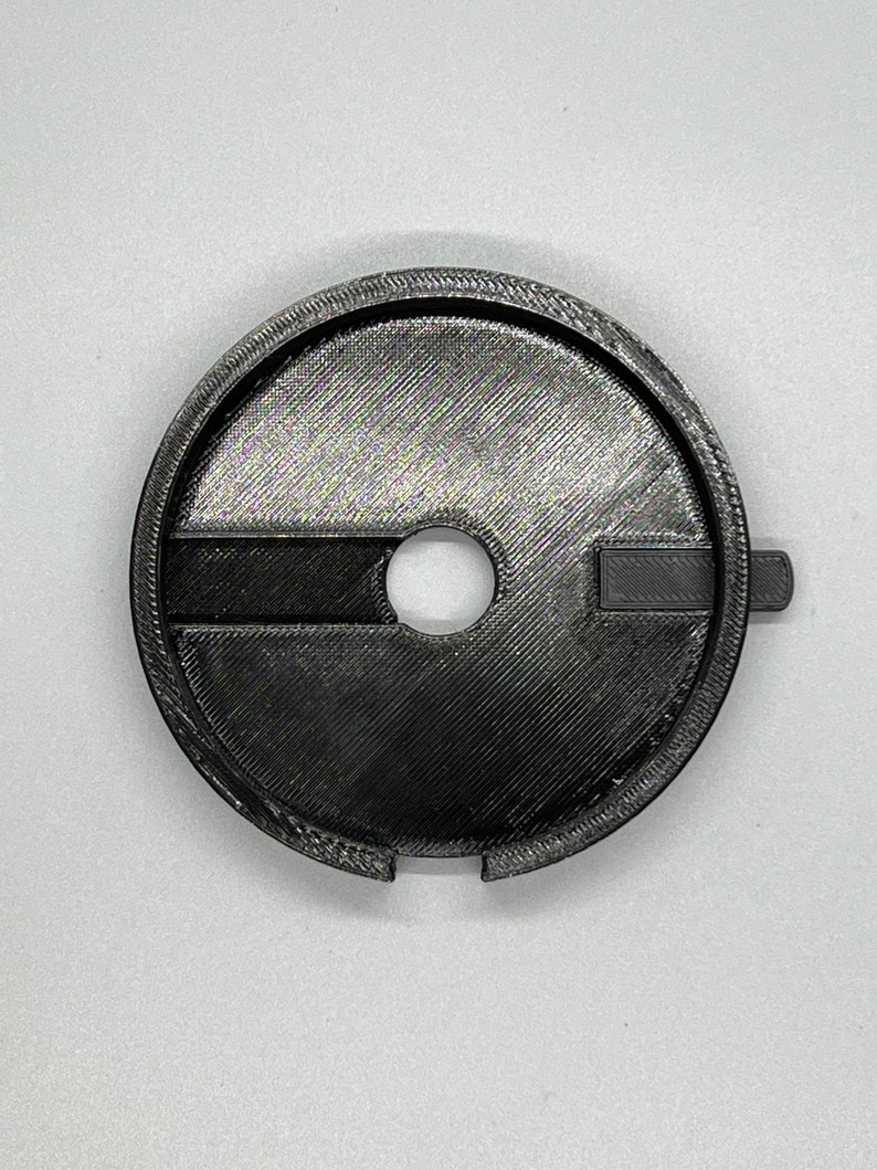May include: A black plastic 3D printed adapter with a circular shape and a small hole in the centre. The adapter has a raised lip around the edge and a small tab on the side.