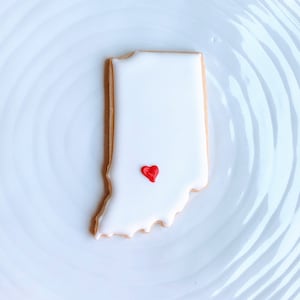 May include: A white cookie decorated with red icing in the shape of the state of Indiana.