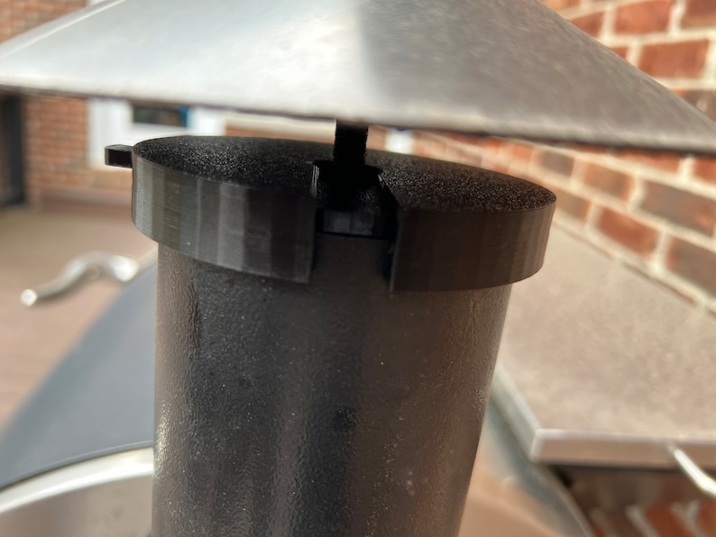 May include: Close-up of a black metal smoker chimney cap with a silver metal rain cover.