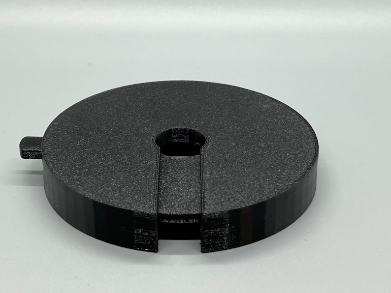 May include: A black plastic ring with a central hole and a split section. The ring is textured and has a matt finish.