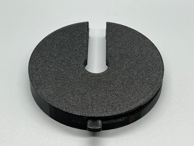 May include: A black plastic ring with a U-shaped opening. The ring is designed to fit around a pipe or other object.