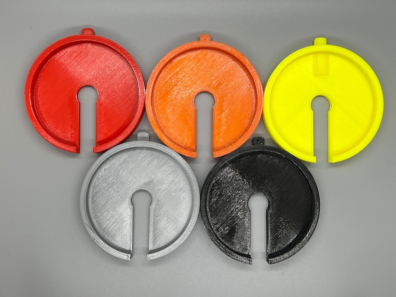 May include: Five round plastic spacers in different colours: red, orange, yellow, grey, and black. Each spacer has a keyhole-shaped opening in the centre.