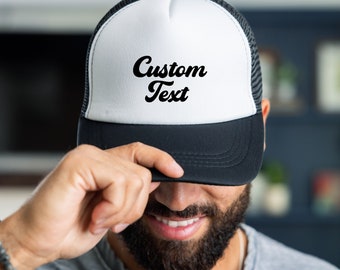 May include: A black and white trucker hat with a white front panel and a black mesh back. The front panel has the text "Custom Text" in a black cursive font.