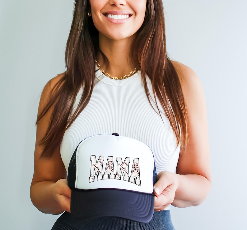 May include: A white and black baseball cap with a mesh back. The front of the cap has the word "MAMA" written in black letters with a baseball stitch design.