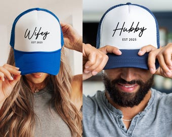 May include: Two trucker hats, one blue and white with the text "Wife EST 2025" and the other navy blue and white with the text "Hubby EST 2025".