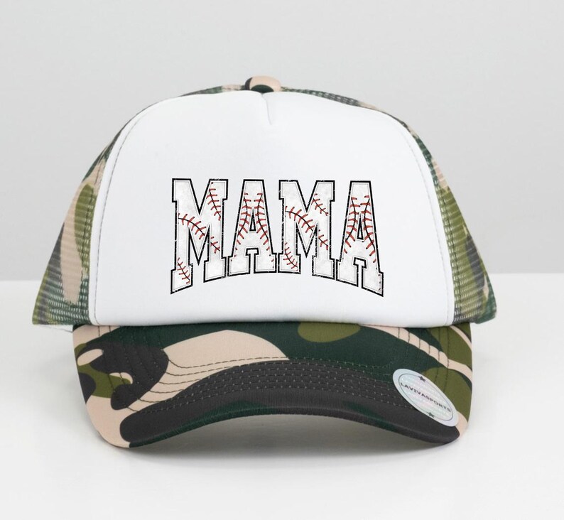 May include: A white trucker hat with a camouflage mesh back. The front of the hat has a white baseball-style graphic with the word "MAMA" in black outlined letters.