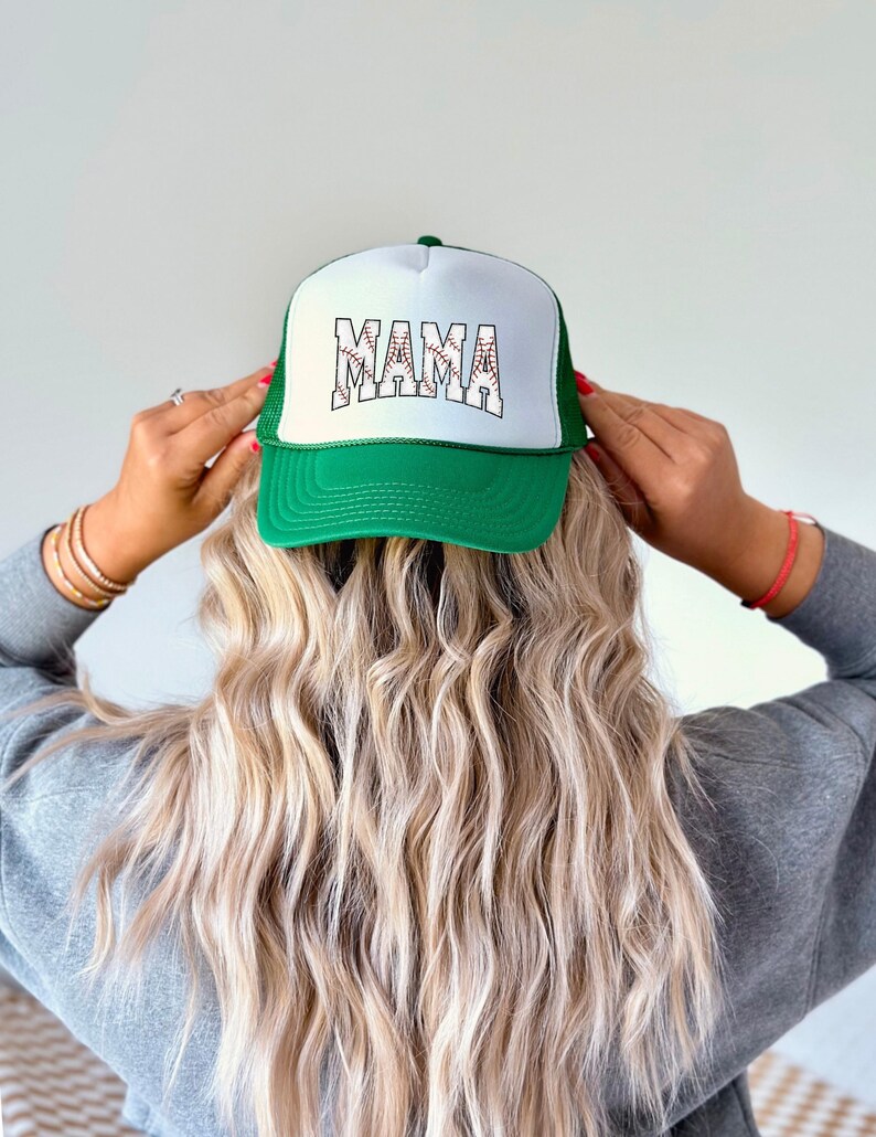 May include: Green and white baseball cap with a white mesh back. The front of the cap has the word "MAMA" written in white letters with a baseball stitch design.