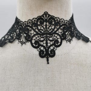 May include: Black lace choker necklace with an intricate floral design. The choker features a detailed pattern with delicate curves and a scalloped edge, creating an elegant and vintage aesthetic. The necklace is displayed on a mannequin.