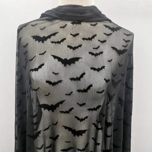 以下が含まれることがあります： 黒いシアー生地に、黒いコウモリのシルエットが繰り返されるパターン。コウモリは様々なサイズで、生地全体に散らばっています。生地はドレープされており、その質感とドレープが強調されています。ハロウィンやゴシック風の作品に最適です。