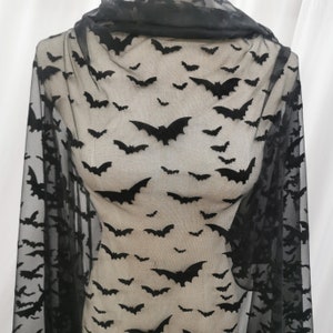 May include: Black sheer fabric featuring a repeating pattern of black bats. The bats are of varying sizes and are spread across the material. The fabric is draped, creating folds and shadows.